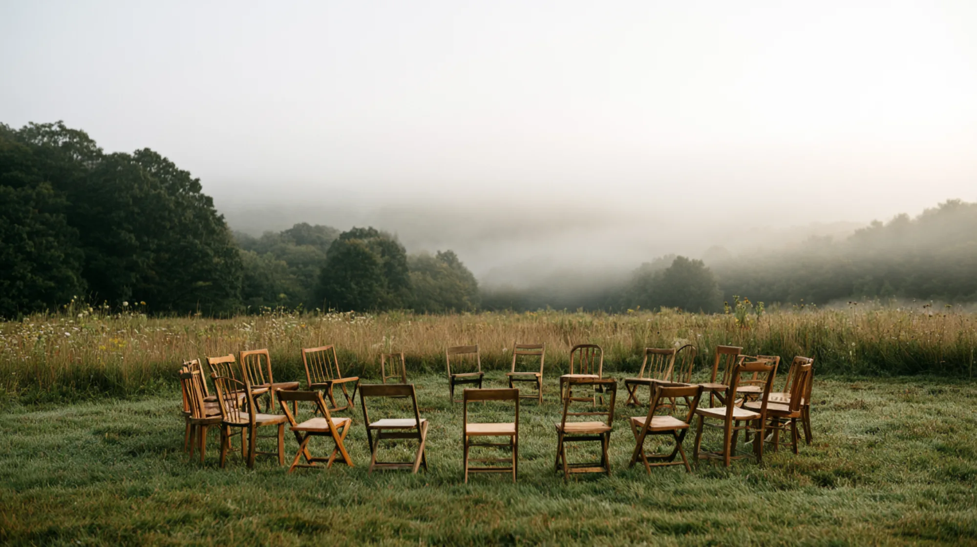 A circle of simple wooden chairs in a misty Finger Lakes meadow at dawn near Ithaca, New York, a meaning-based gathering space for therapy groups with Laurie Buehler, MFT